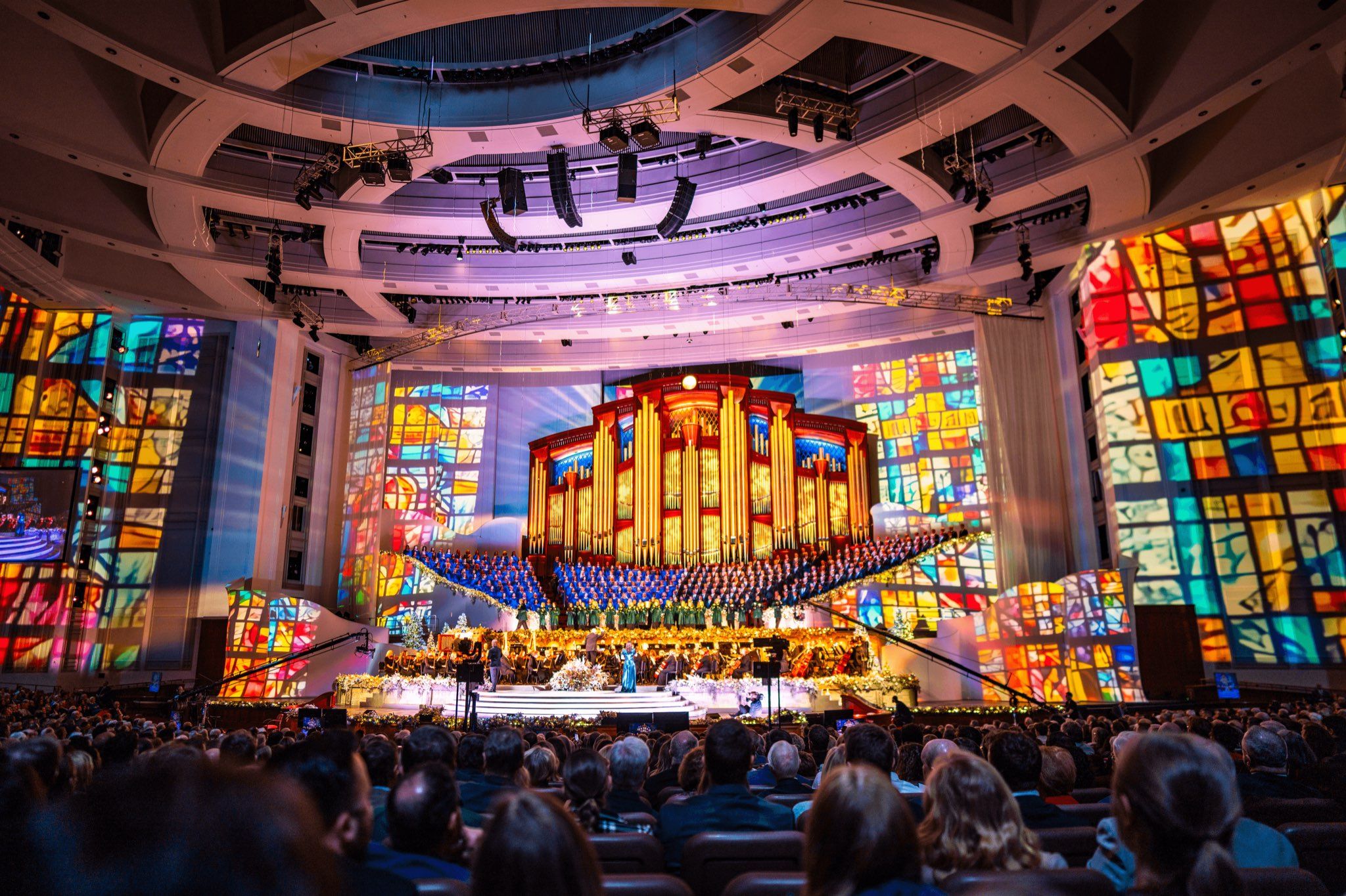 The Tabernacle Choir at Temple Square and the Orchestra at Temple Square performing their annual Christmas concert in the Conference Center, the hall lit warm against a darkened auditorium.